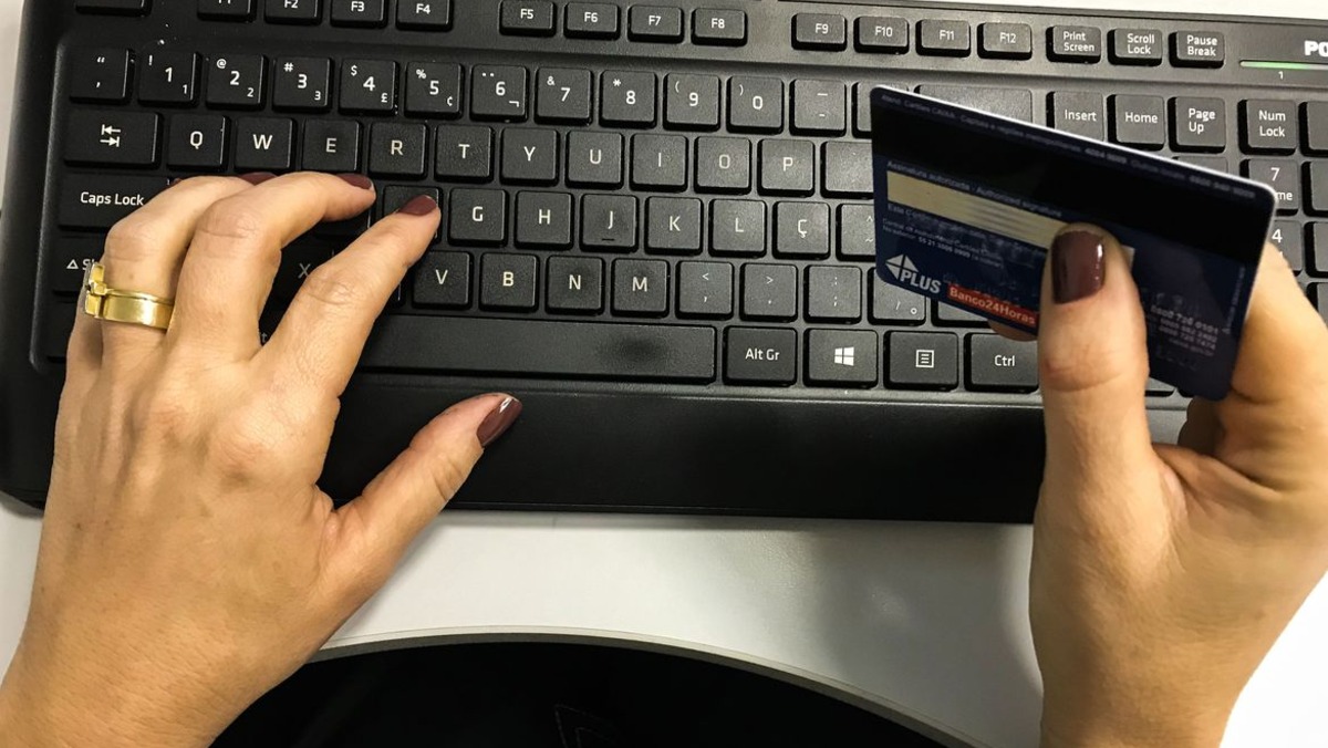 mão feminina digitando no teclado com cartão bancário