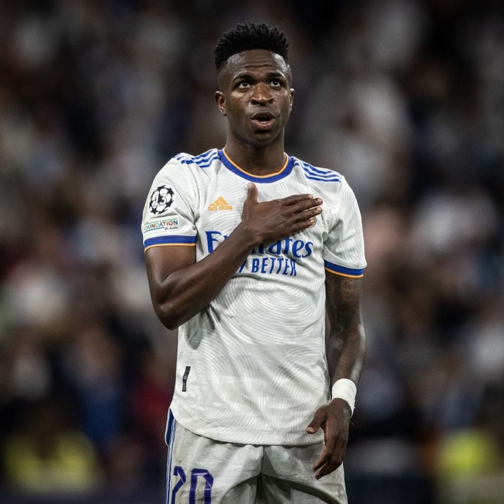 Vini Jr veste a camisa branca do Real Madrid, e coloca a mão direita no coração