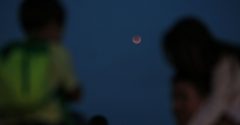 Duas pessoas observam a lua no céu ao entardecer