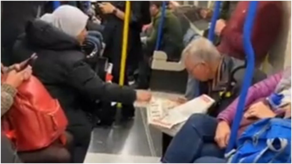 jovem ajuda idoso com parkinson a ler jornal em metrô