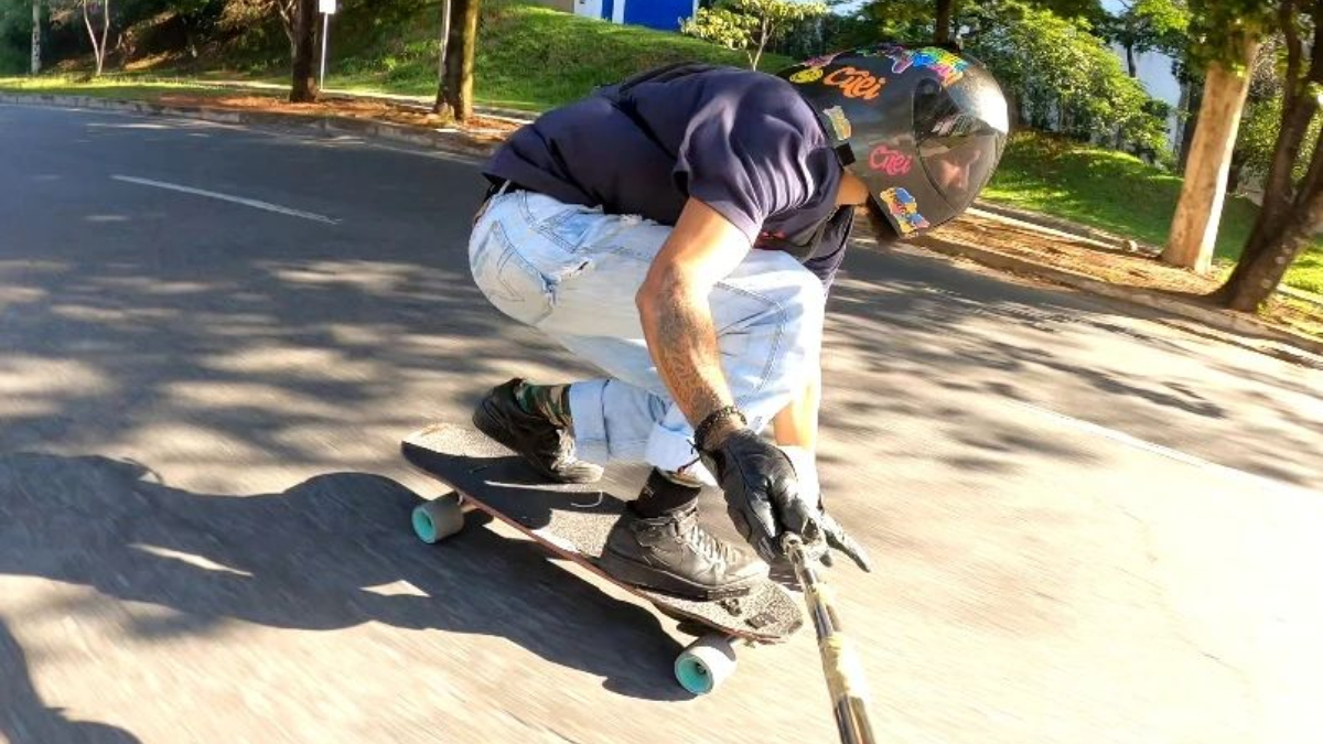 atleta descendo morro de skate em alta velocidade e segurando uma câmera