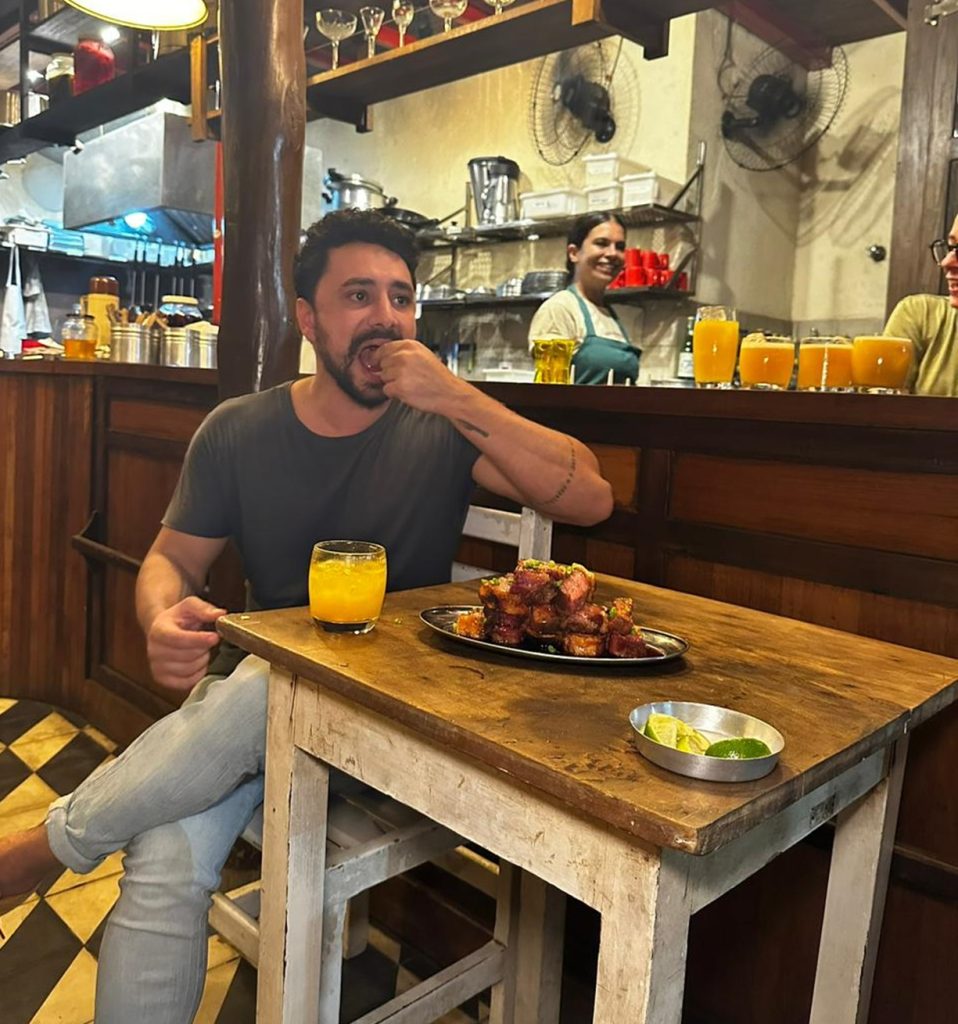 Eu feliz com uma porção de torresmo e um drink à base de cachaça, na Casa Alvorada.